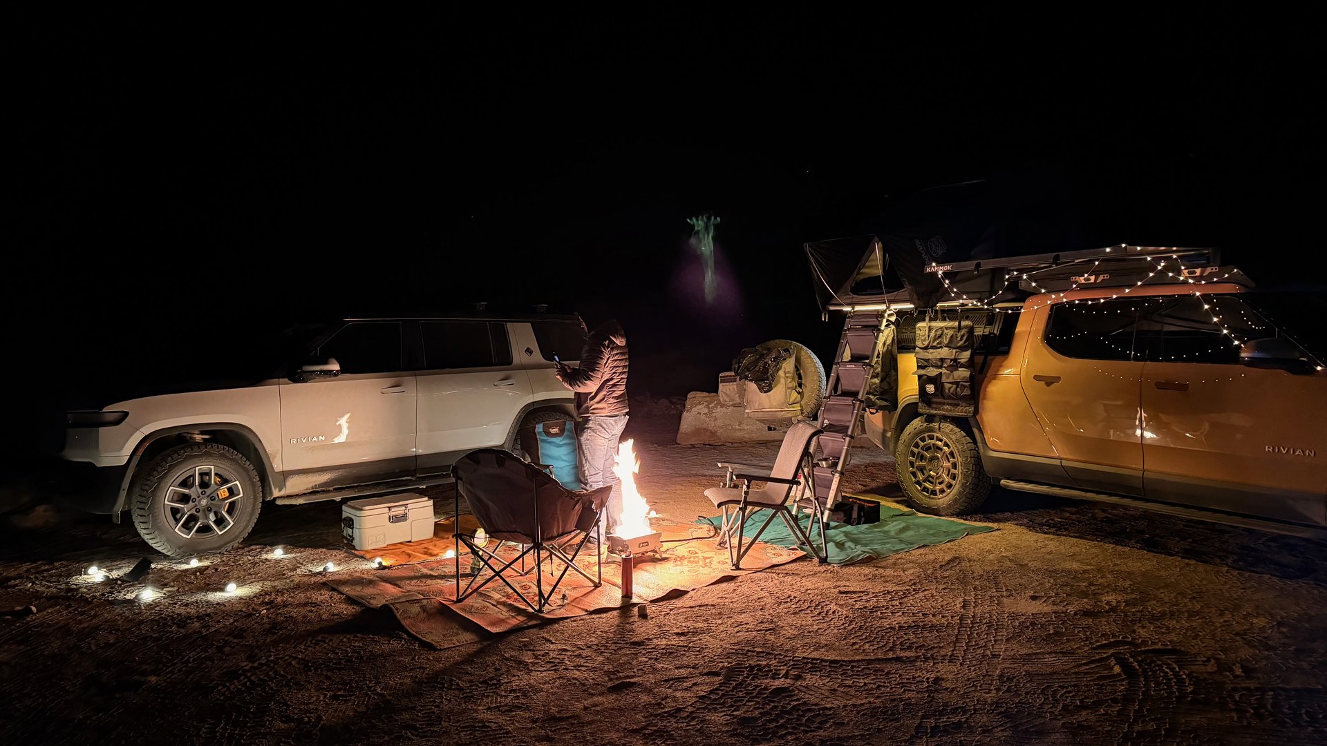 Two Rivian trucks at a desert campsite at night