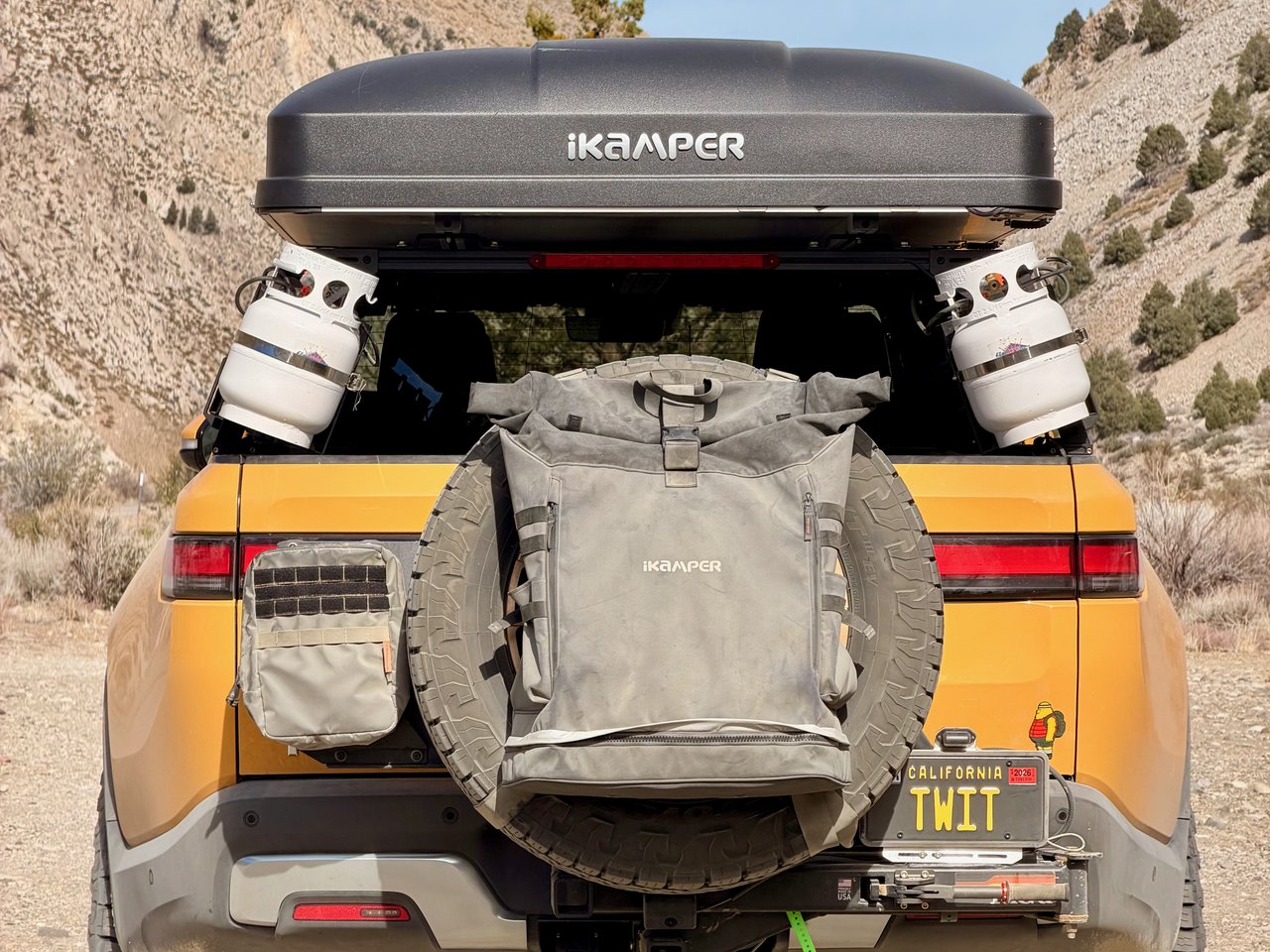 Rear view of the Rivian with a rooftop tent, spare tire, and camp gear