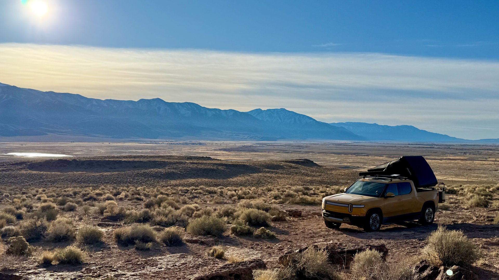 Yellow Rivian R1T with rooftop tent in a broad mountain landscape