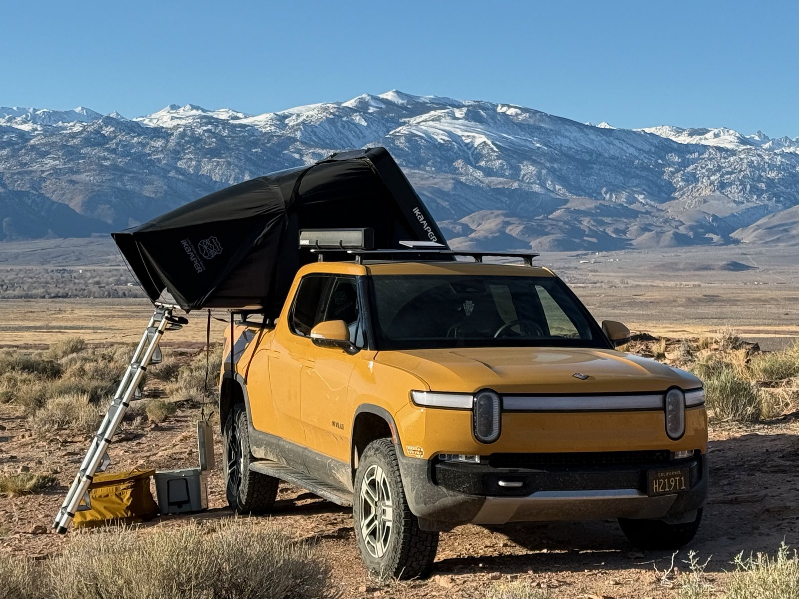 Rivian R1T with rooftop tent open in front of snowy mountains