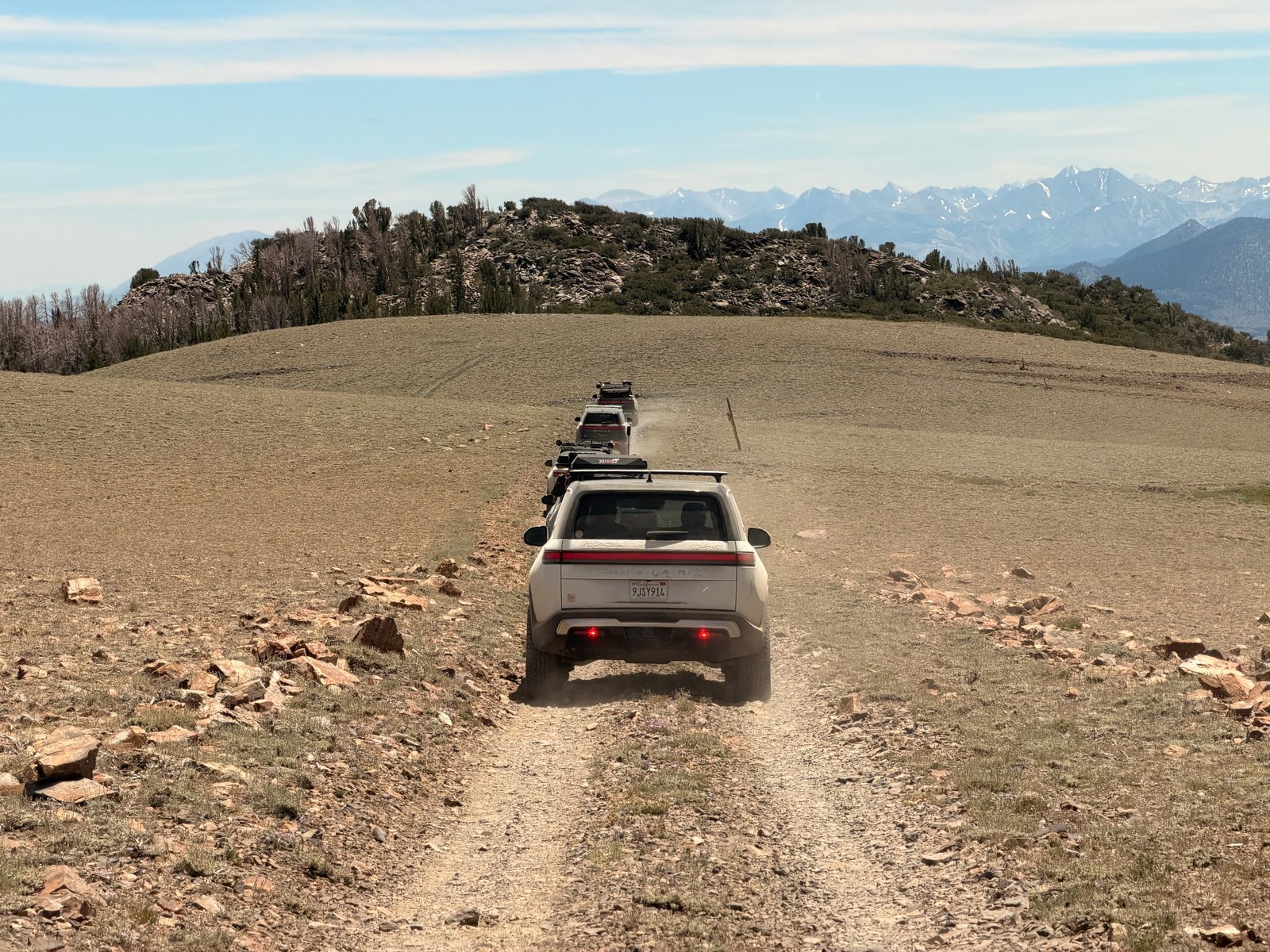 A line of Rivian trucks traveling a rocky mountain trail