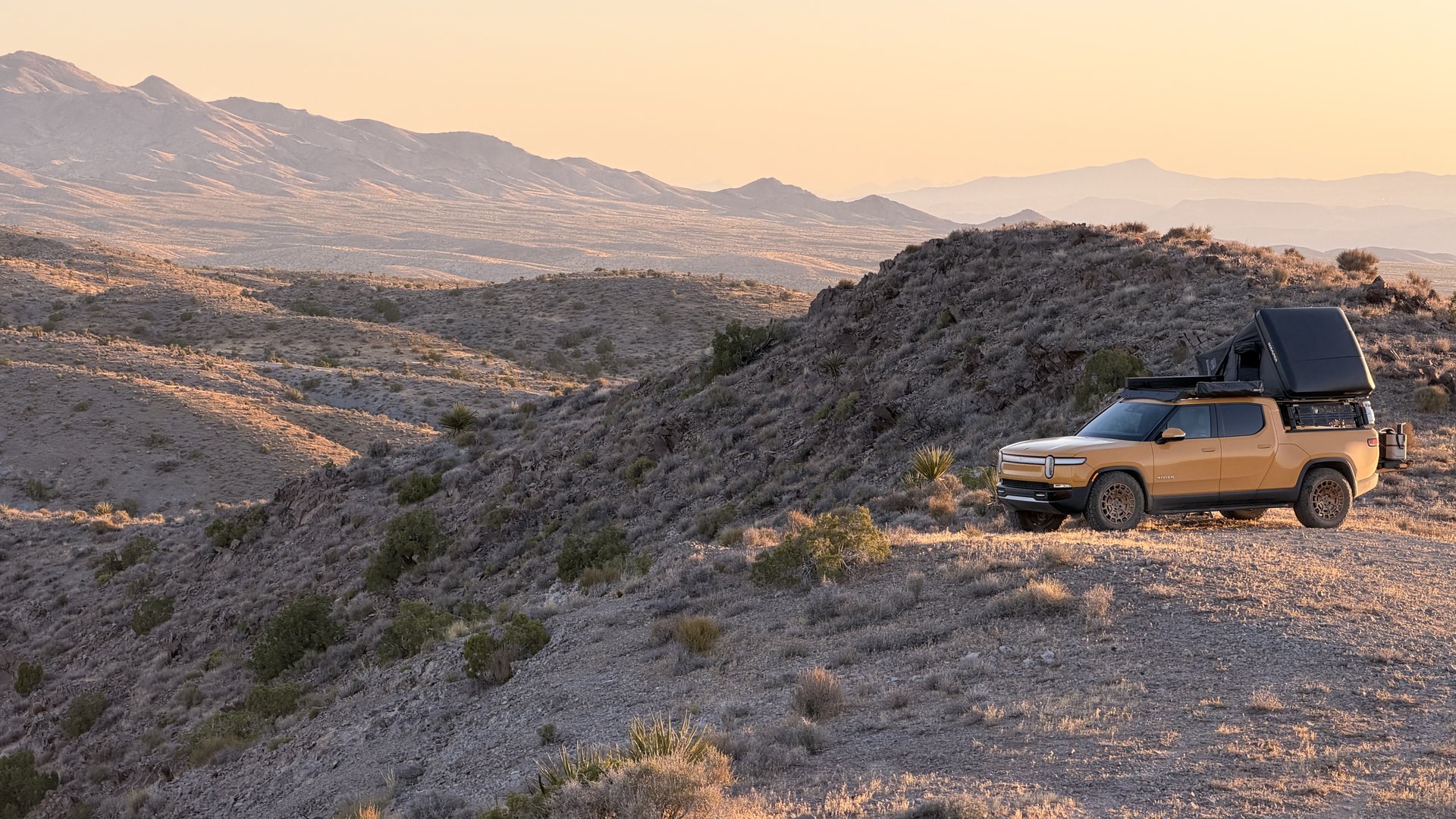 Golden Rivian R1T on a desert ridge at sunset